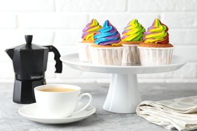 Photo of Delicious cupcakes with colorful cream and cup of coffee on grey textured table, closeup