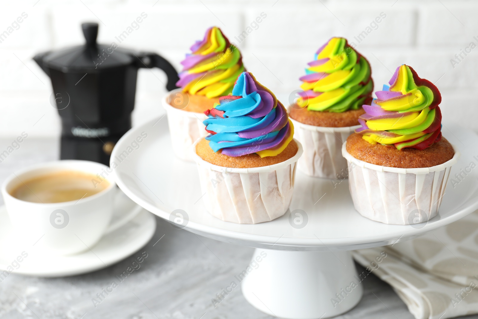 Photo of Delicious cupcakes with colorful cream and cup of coffee on grey table, closeup