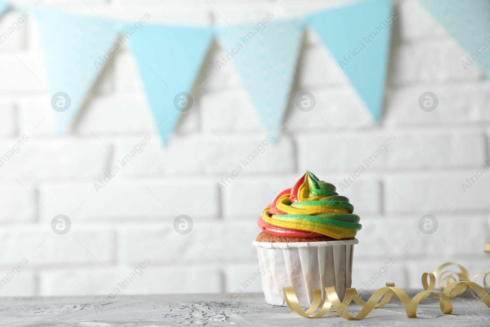 Photo of Delicious cupcake with colorful cream on grey textured table near white brick wall. Space for text