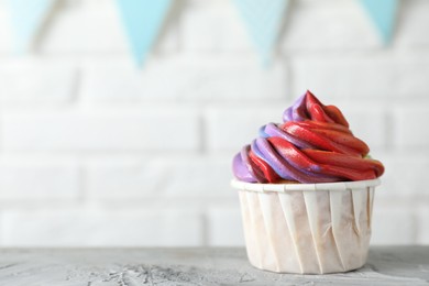 Photo of Delicious cupcake with colorful cream on grey textured table against blurred background, closeup. Space for text