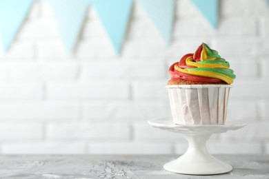 Photo of Delicious cupcake with colorful cream on grey textured table against blurred background, closeup. Space for text