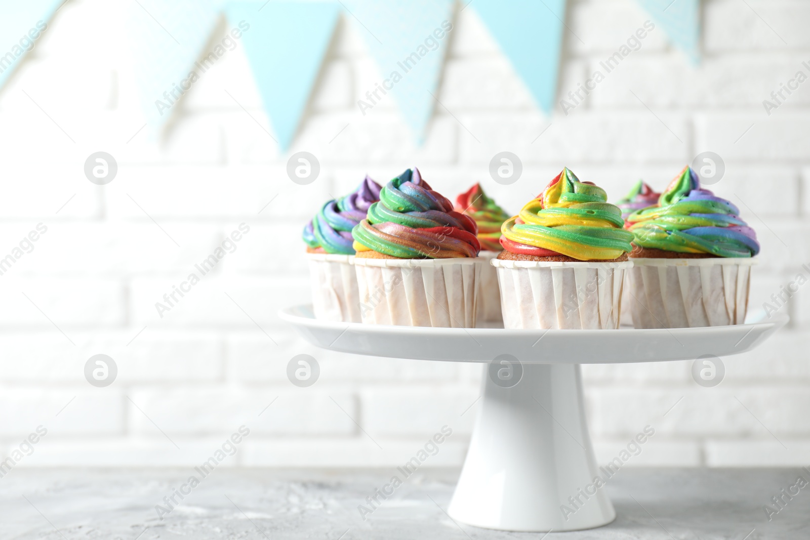 Photo of Delicious cupcakes with colorful cream on grey textured table near white brick wall, closeup. Space for text