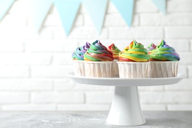 Photo of Delicious cupcakes with colorful cream on grey textured table near white brick wall, closeup. Space for text