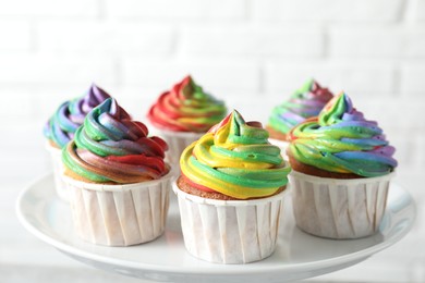 Photo of Delicious cupcakes with colorful cream on stand against blurred background, closeup