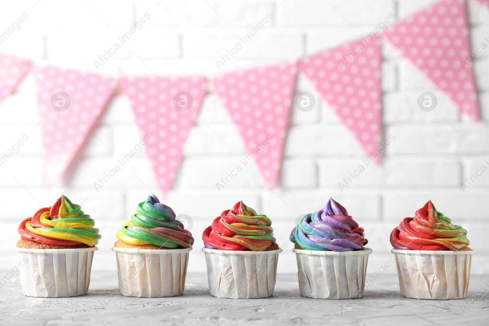 Photo of Delicious cupcakes with colorful cream on grey textured table near white brick wall, closeup. Space for text