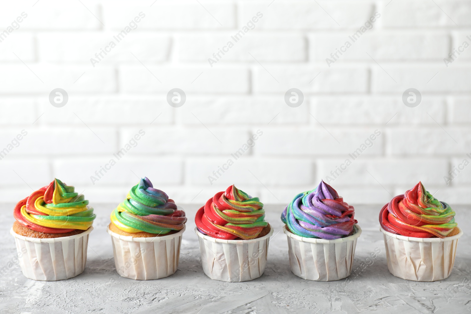 Photo of Delicious cupcakes with colorful cream on grey textured table near white brick wall, closeup. Space for text