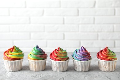 Photo of Delicious cupcakes with colorful cream on grey textured table near white brick wall, closeup. Space for text