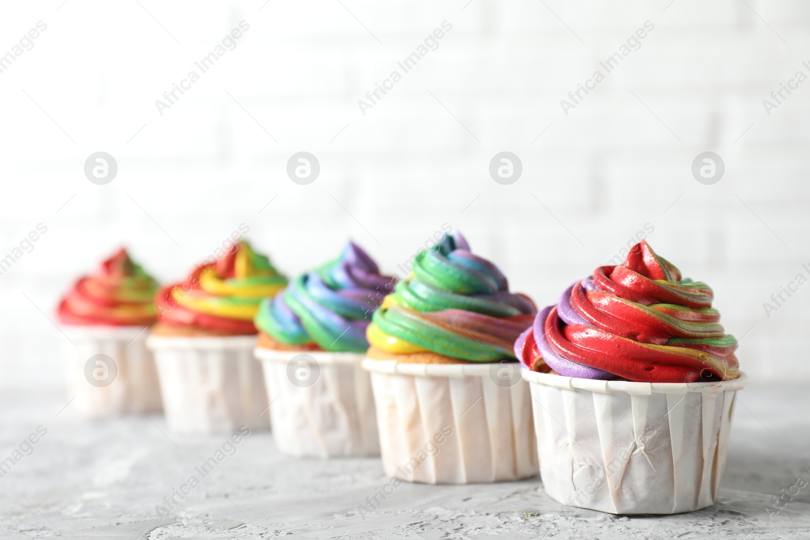 Photo of Delicious cupcakes with colorful cream on grey textured table near white wall, closeup