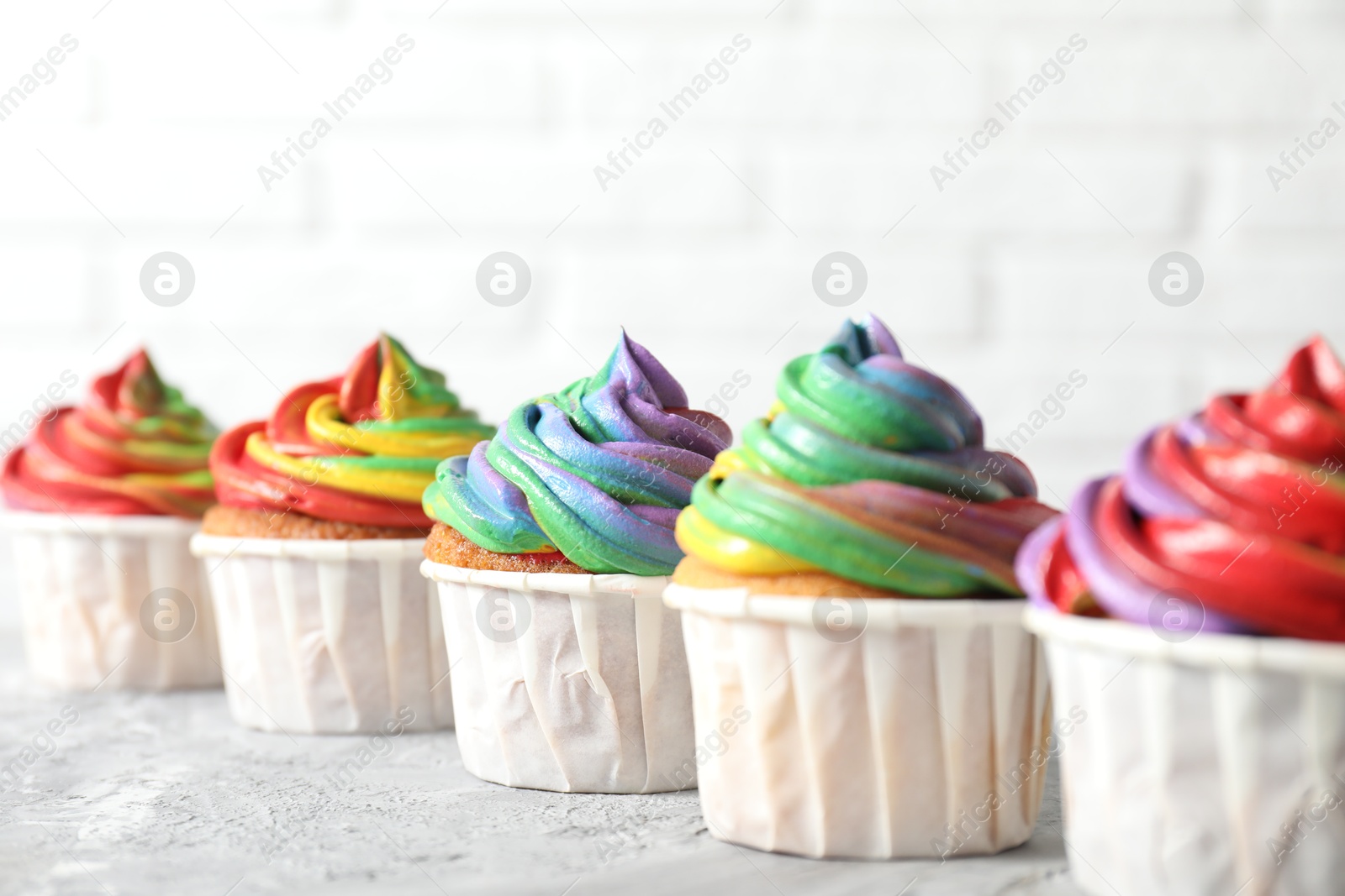 Photo of Delicious cupcakes with colorful cream on grey textured table near white wall, closeup