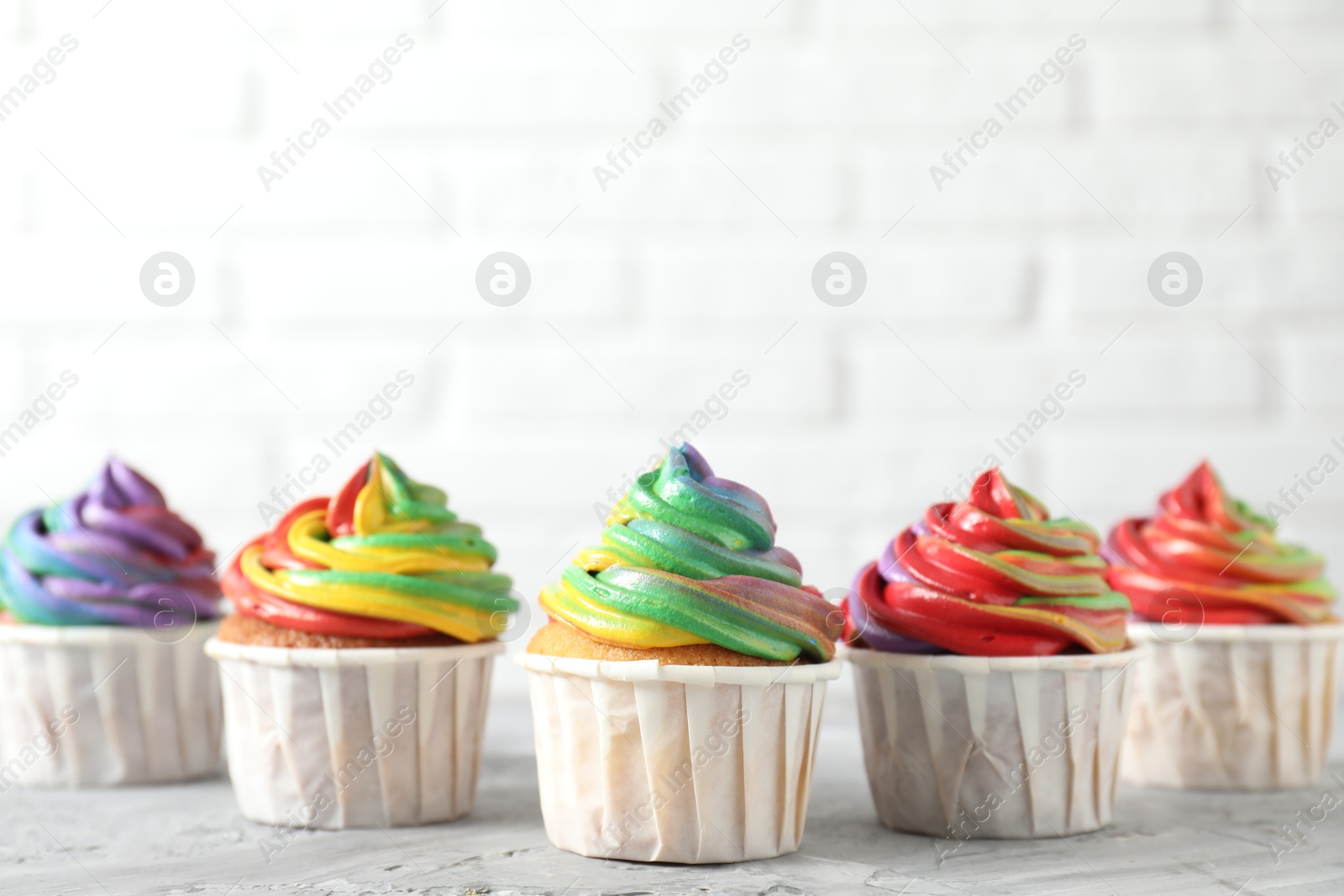 Photo of Delicious cupcakes with colorful cream on grey textured table near white wall, closeup. Space for text