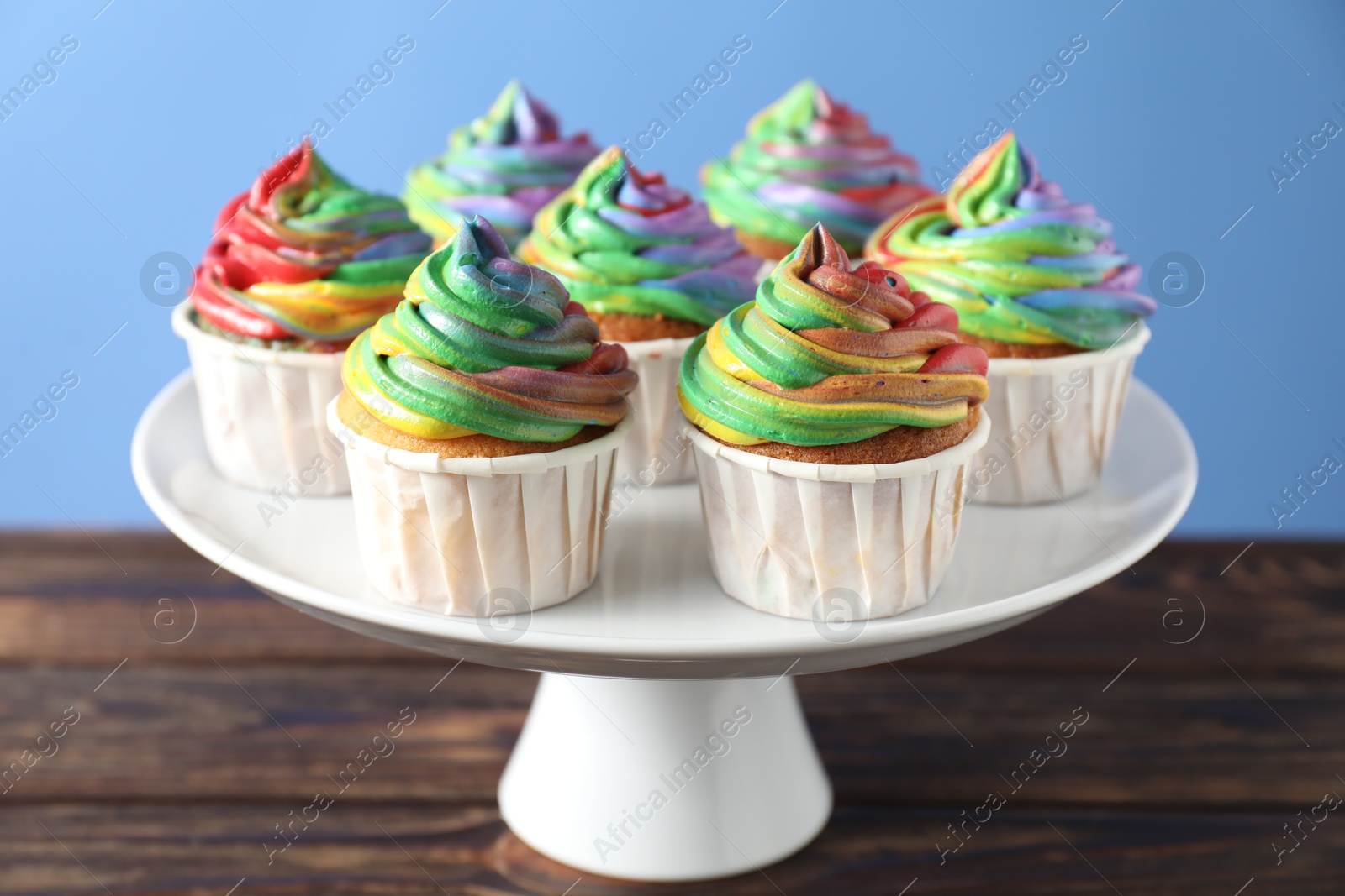 Photo of Delicious cupcakes with colorful cream on wooden table against blue background, closeup