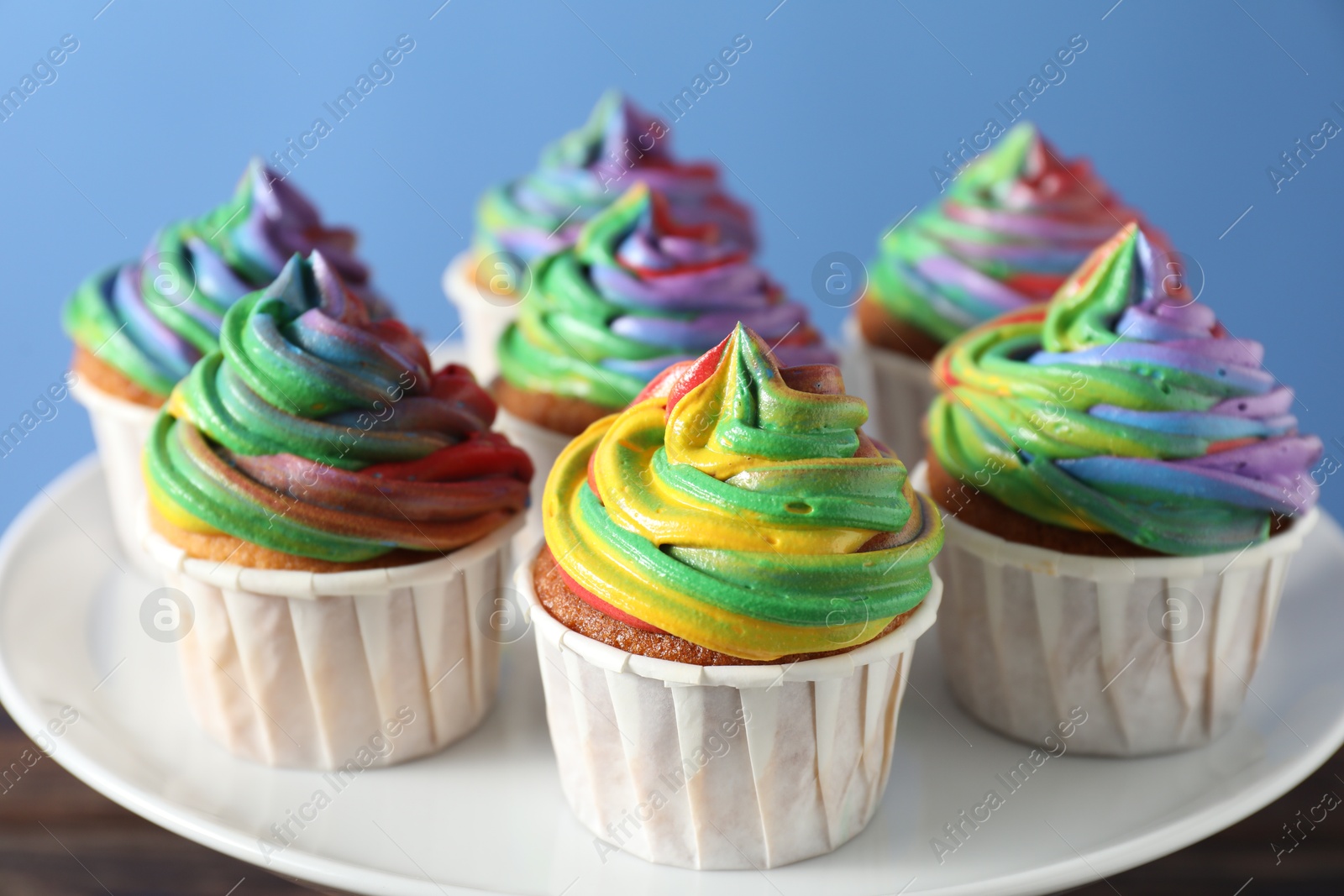 Photo of Delicious cupcakes with colorful cream on stand against blue background, closeup