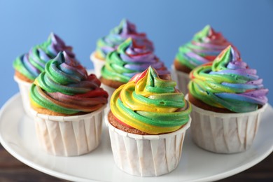 Photo of Delicious cupcakes with colorful cream on stand against blue background, closeup