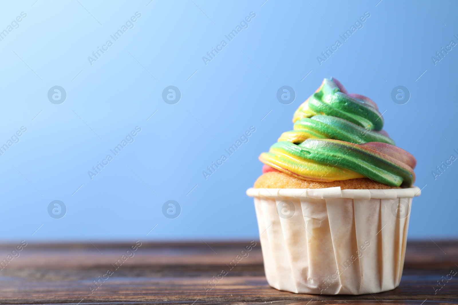 Photo of Delicious cupcake with colorful cream on wooden table against blue background, closeup. Space for text