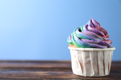 Photo of Delicious cupcake with colorful cream on wooden table against blue background, closeup. Space for text