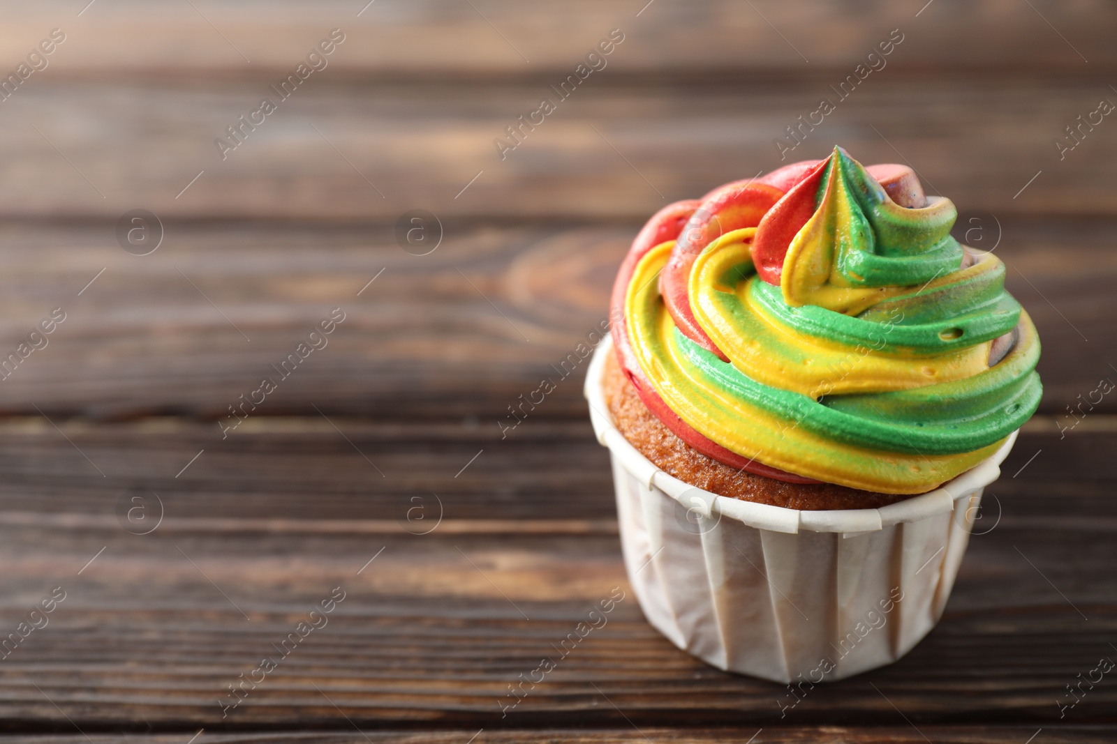 Photo of Delicious cupcake with colorful cream on wooden table, closeup. Space for text