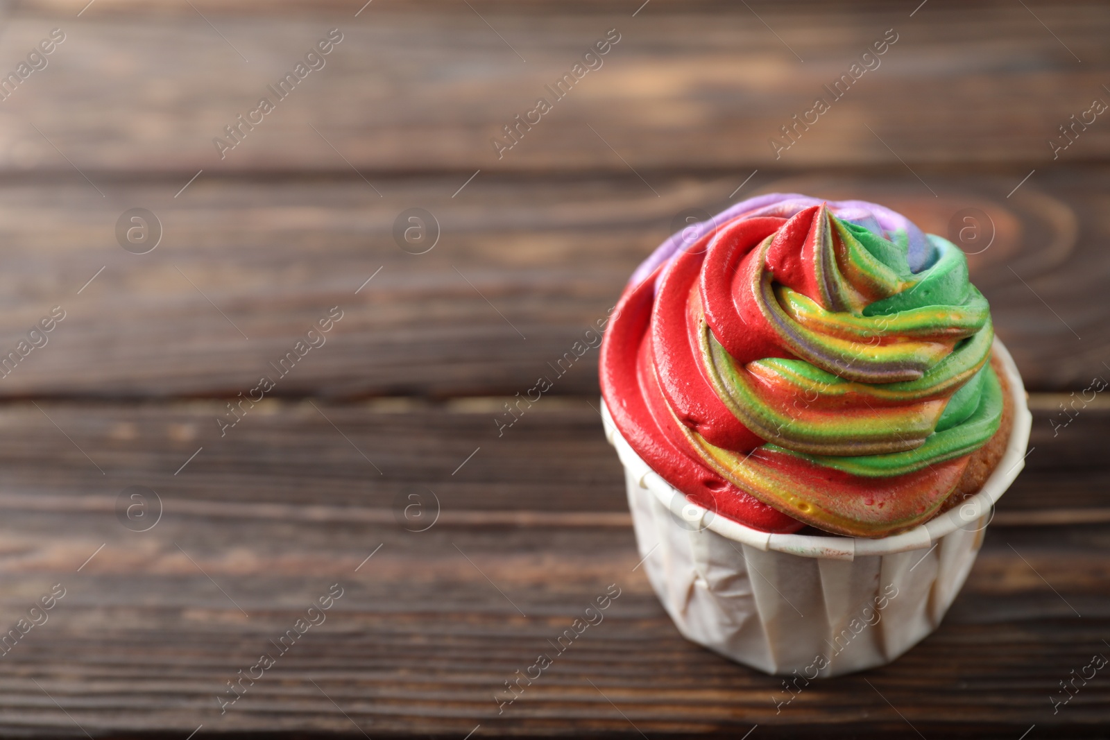 Photo of Delicious cupcake with colorful cream on wooden table, closeup. Space for text