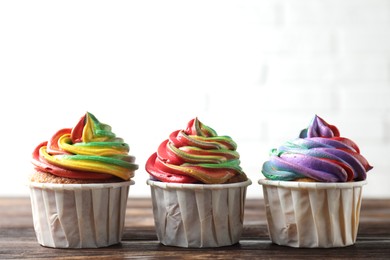 Photo of Delicious cupcakes with colorful cream on wooden table against white background, closeup