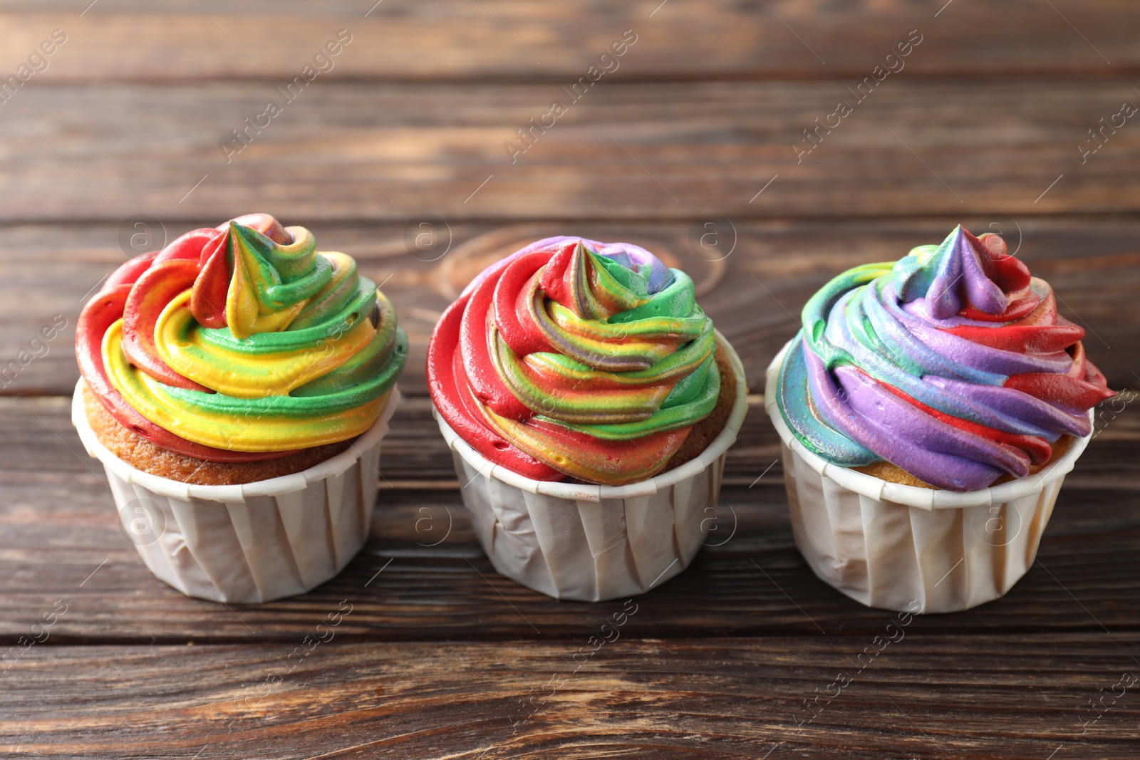 Photo of Delicious cupcakes with colorful cream on wooden table, closeup