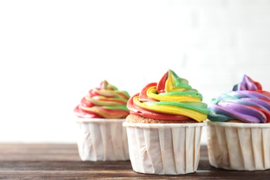 Photo of Delicious cupcakes with colorful cream on wooden table against white background, closeup. Space for text