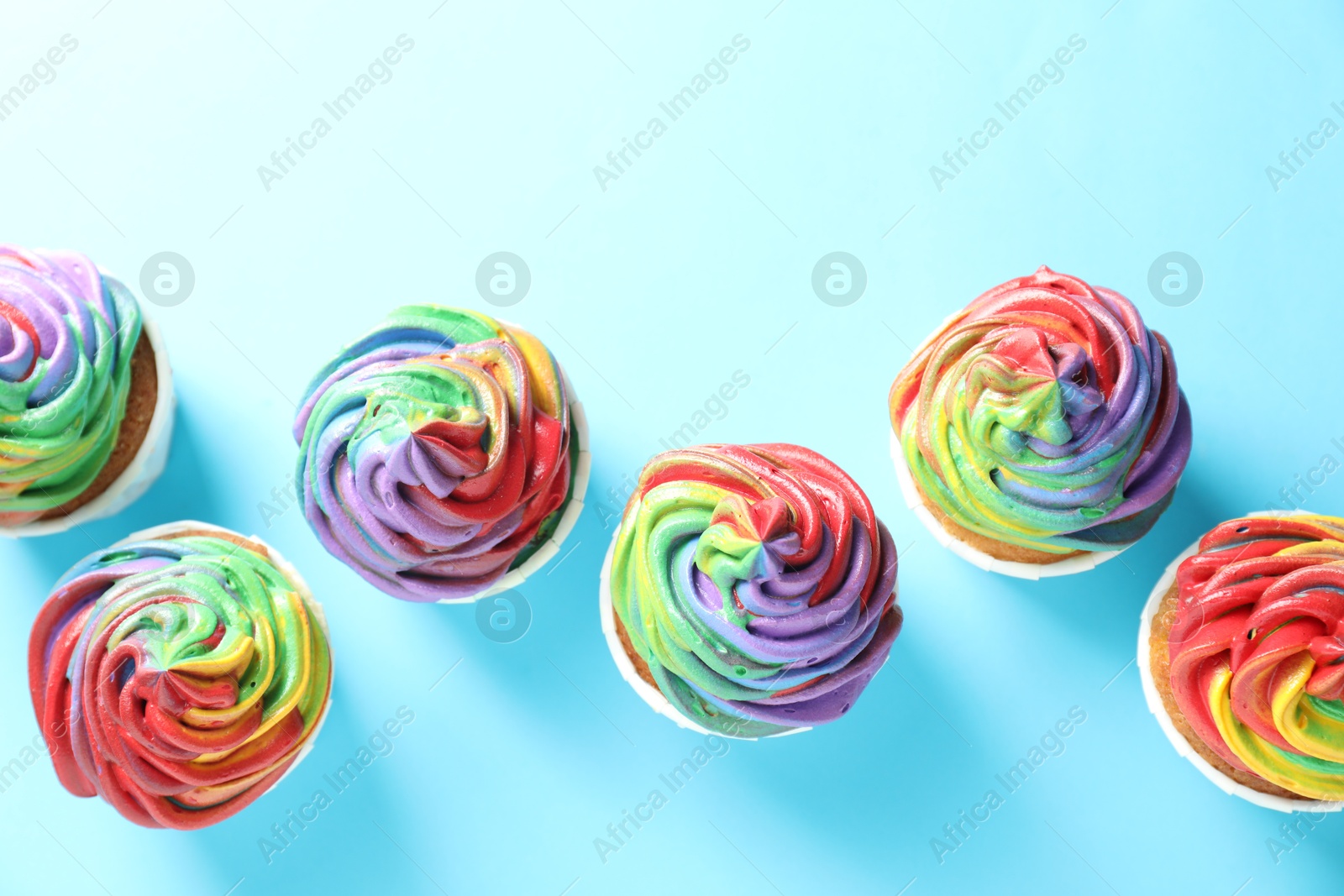 Photo of Delicious cupcakes with colorful cream on light blue background, flat lay