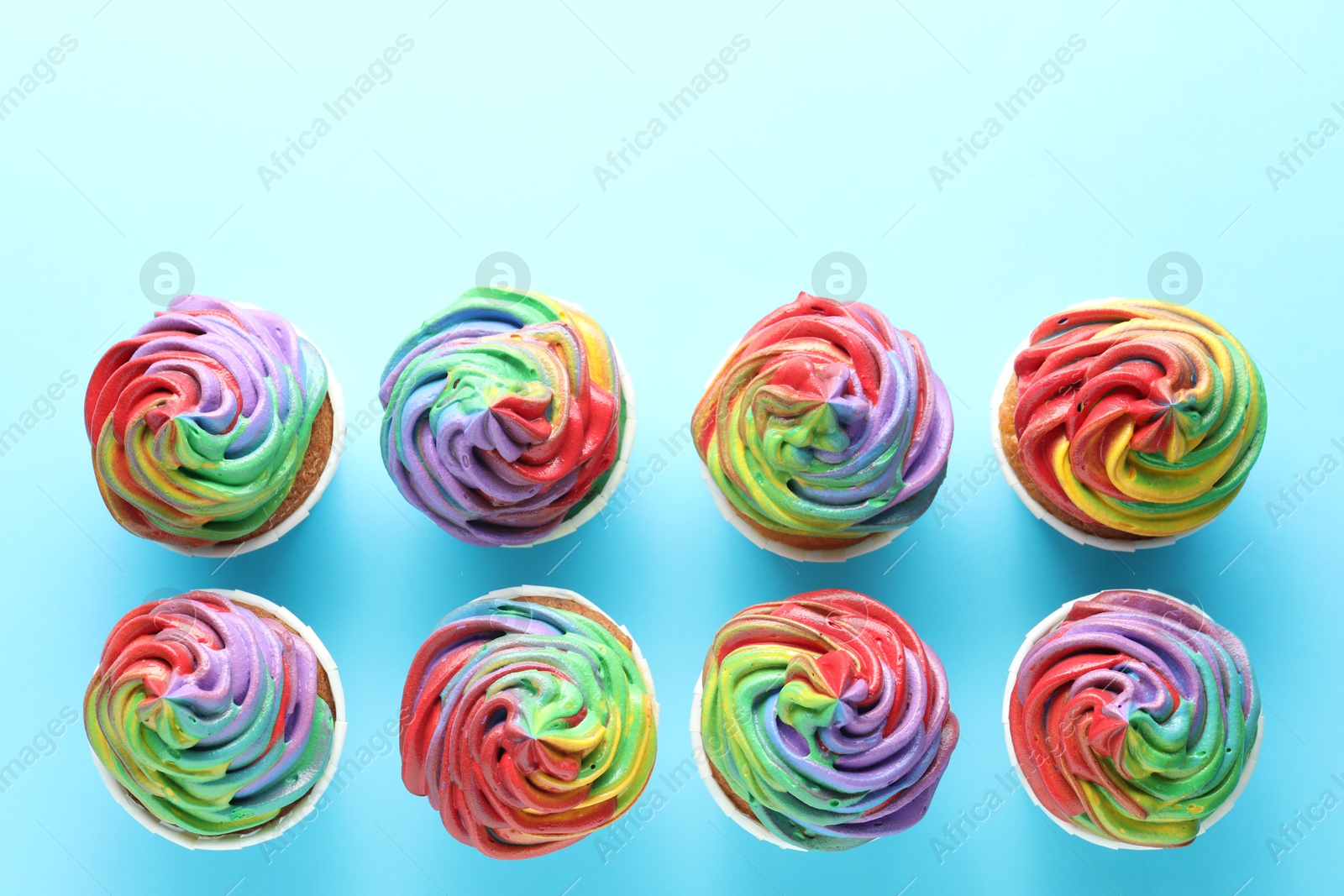 Photo of Delicious cupcakes with colorful cream on light blue background, flat lay