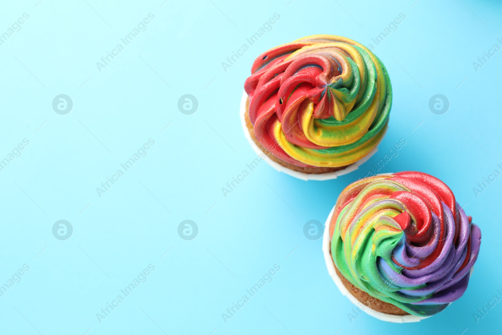 Photo of Delicious cupcakes with colorful cream on light blue background, flat lay. Space for text