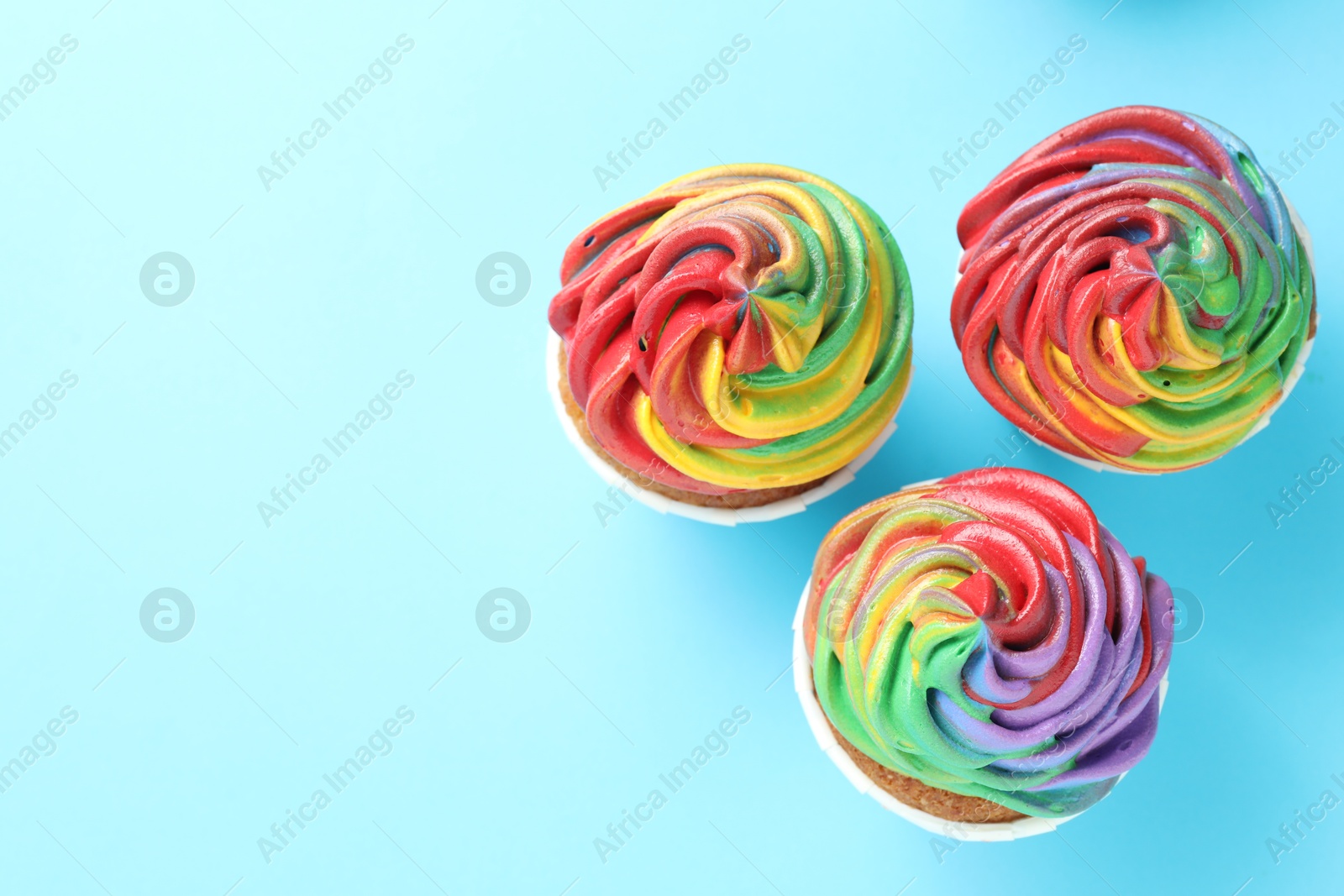 Photo of Delicious cupcakes with colorful cream on light blue background, flat lay. Space for text