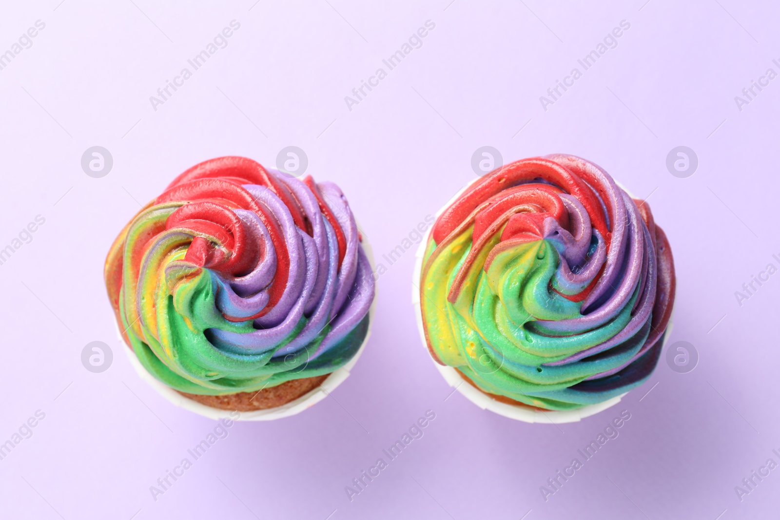 Photo of Delicious cupcakes with colorful cream on violet background, flat lay