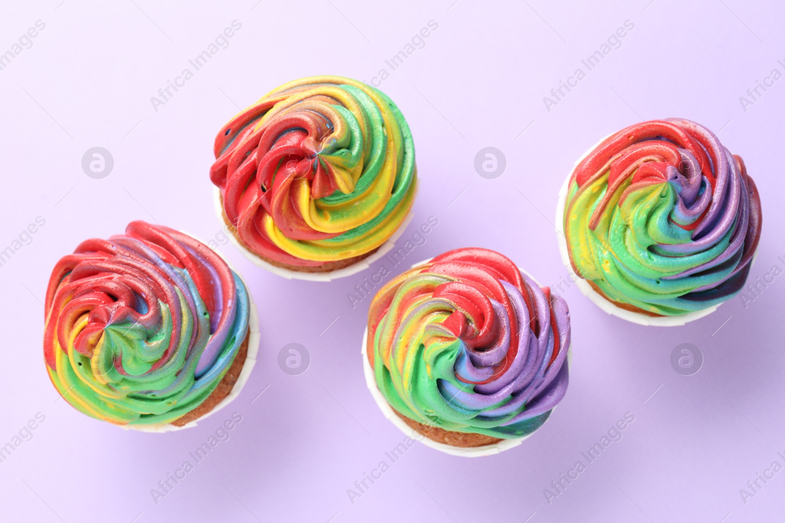 Photo of Delicious cupcakes with colorful cream on violet background, flat lay