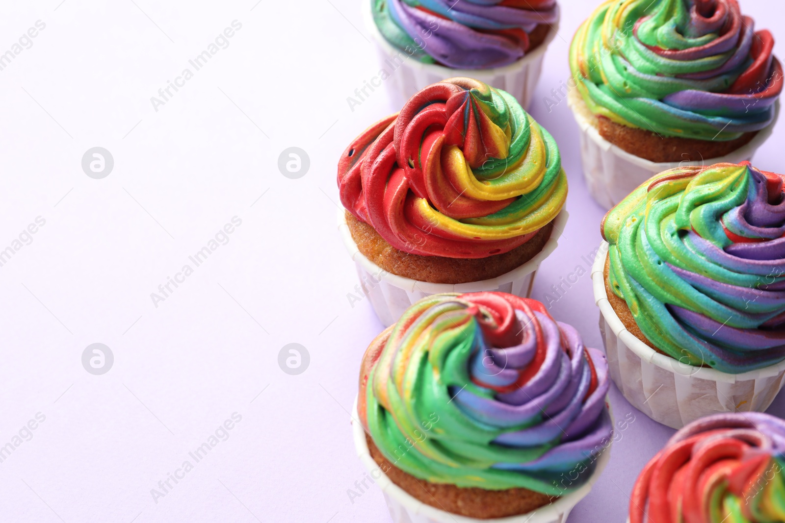 Photo of Delicious cupcakes with colorful cream on violet background, closeup. Space for text