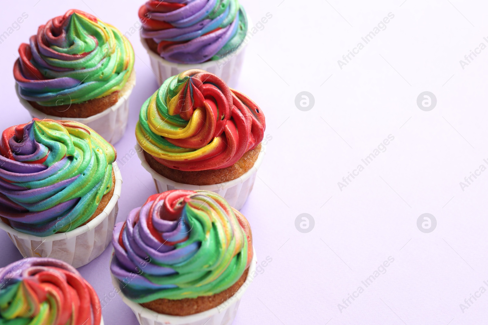 Photo of Delicious cupcakes with colorful cream on violet background, closeup. Space for text