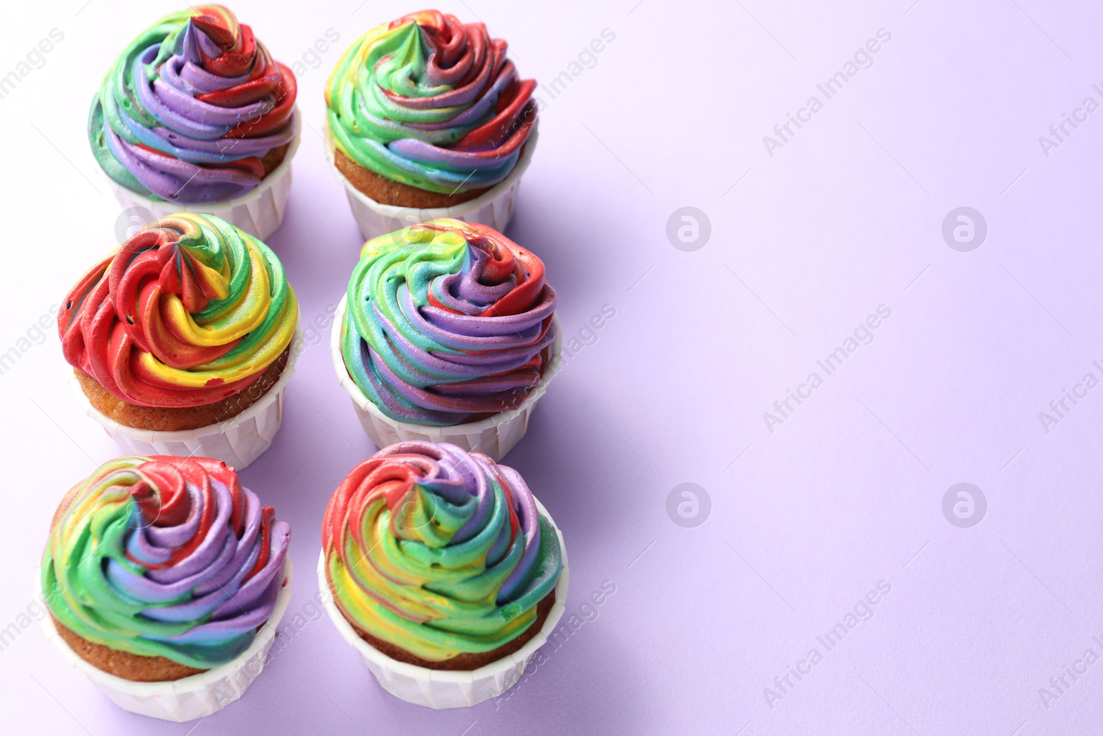 Photo of Delicious cupcakes with colorful cream on violet background. Space for text