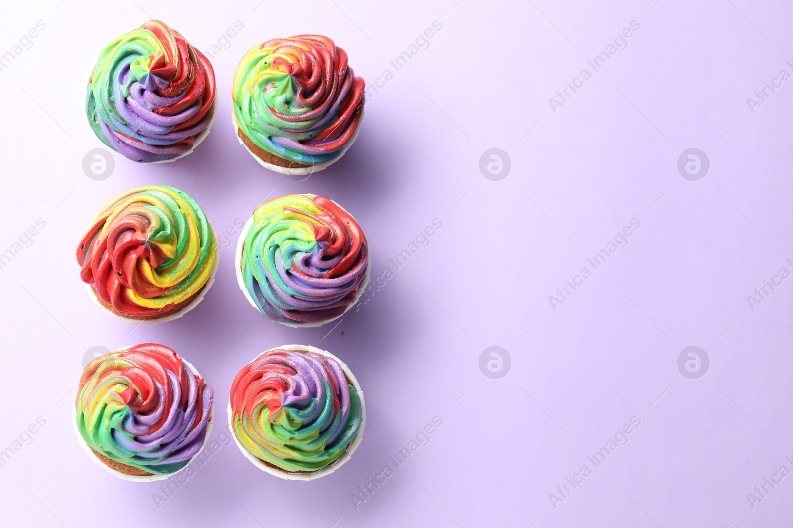 Photo of Delicious cupcakes with colorful cream on violet background, flat lay. Space for text