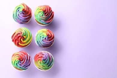 Photo of Delicious cupcakes with colorful cream on violet background, flat lay. Space for text