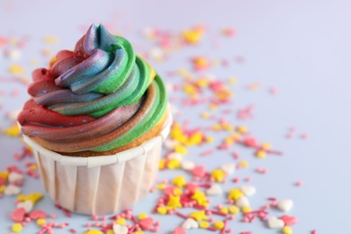 Photo of Delicious cupcake with colorful cream and confetti on light table, closeup. Space for text