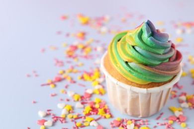 Photo of Delicious cupcake with colorful cream and confetti on light table, closeup. Space for text