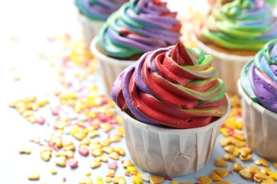 Photo of Delicious cupcakes with colorful cream and confetti on light table, closeup. Space for text