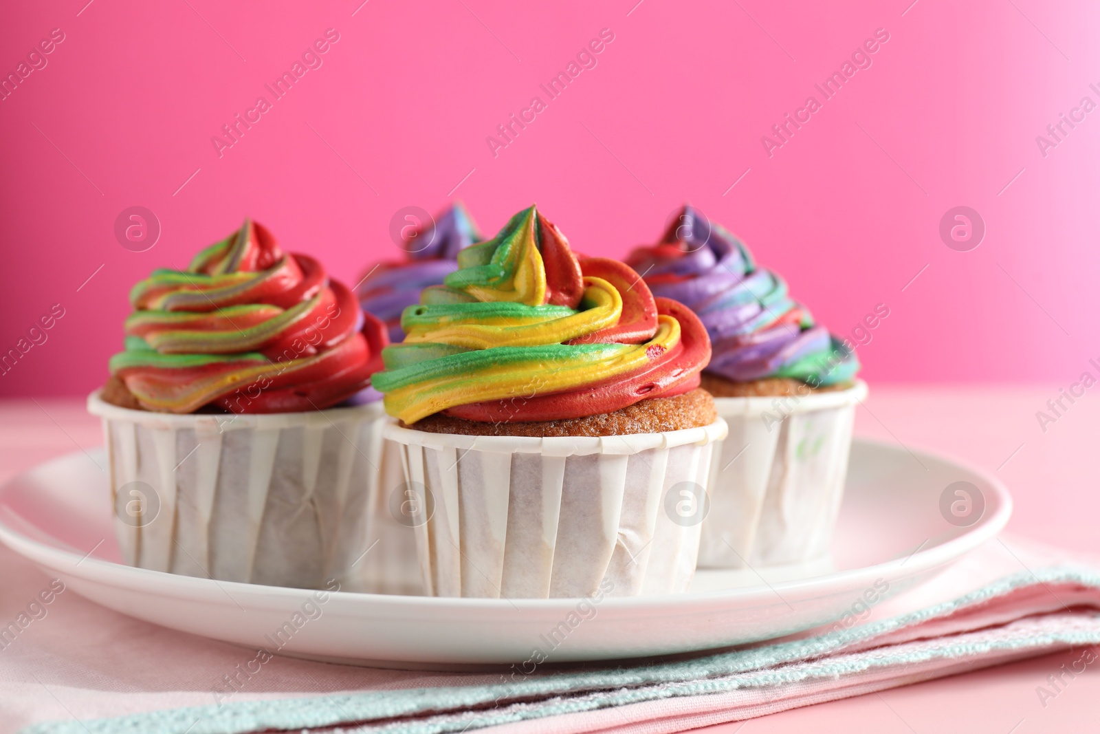 Photo of Delicious cupcakes with colorful cream on pink table, closeup