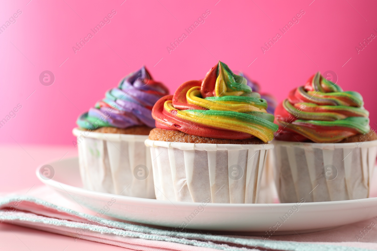 Photo of Delicious cupcakes with colorful cream on pink table, closeup