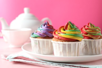 Photo of Delicious cupcakes with colorful cream and tea on pink table, closeup