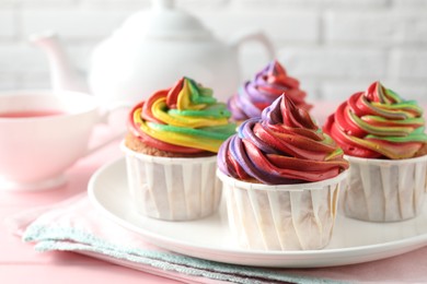 Photo of Delicious cupcakes with colorful cream and tea on pink table, closeup