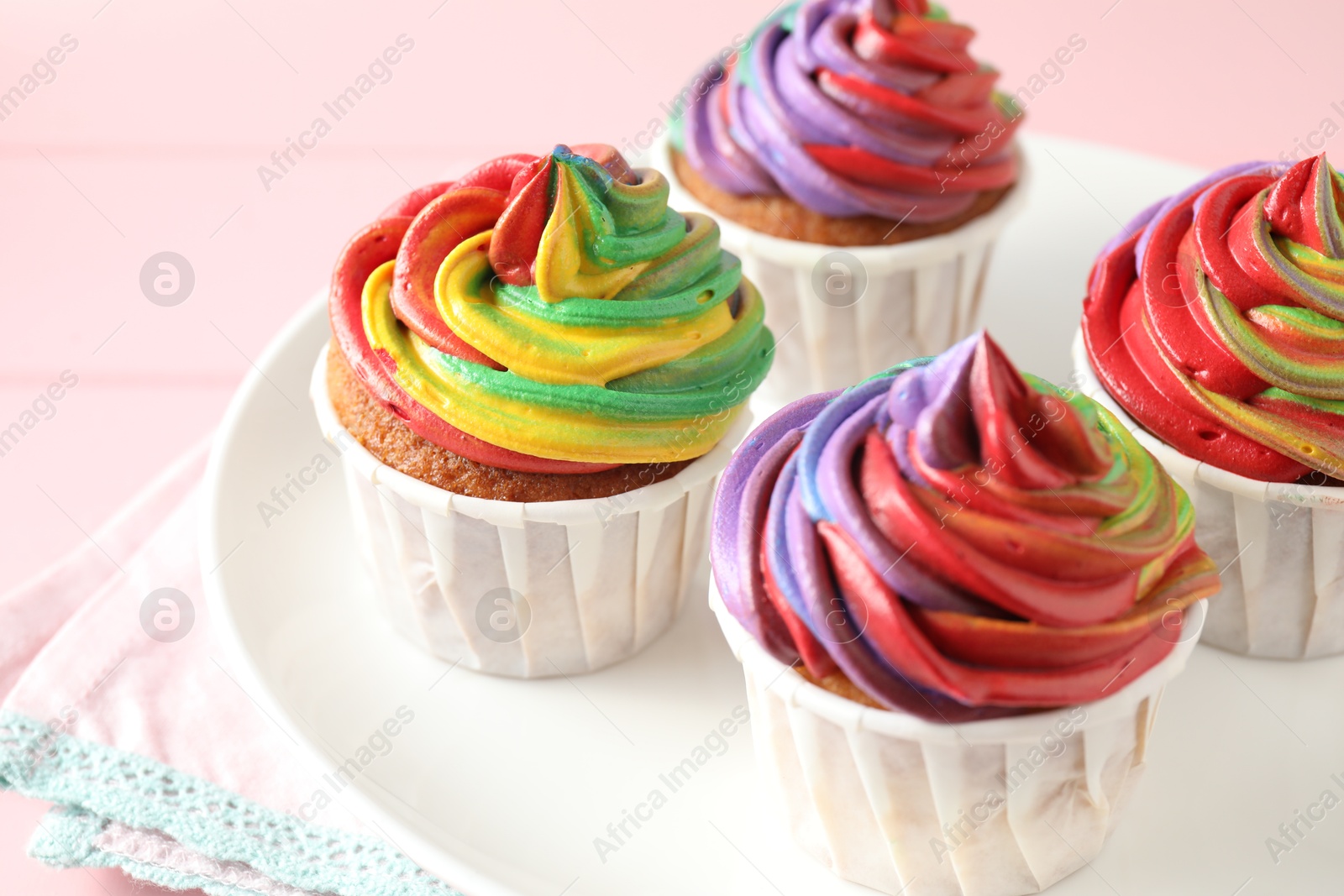 Photo of Delicious cupcakes with colorful cream on pink table, closeup