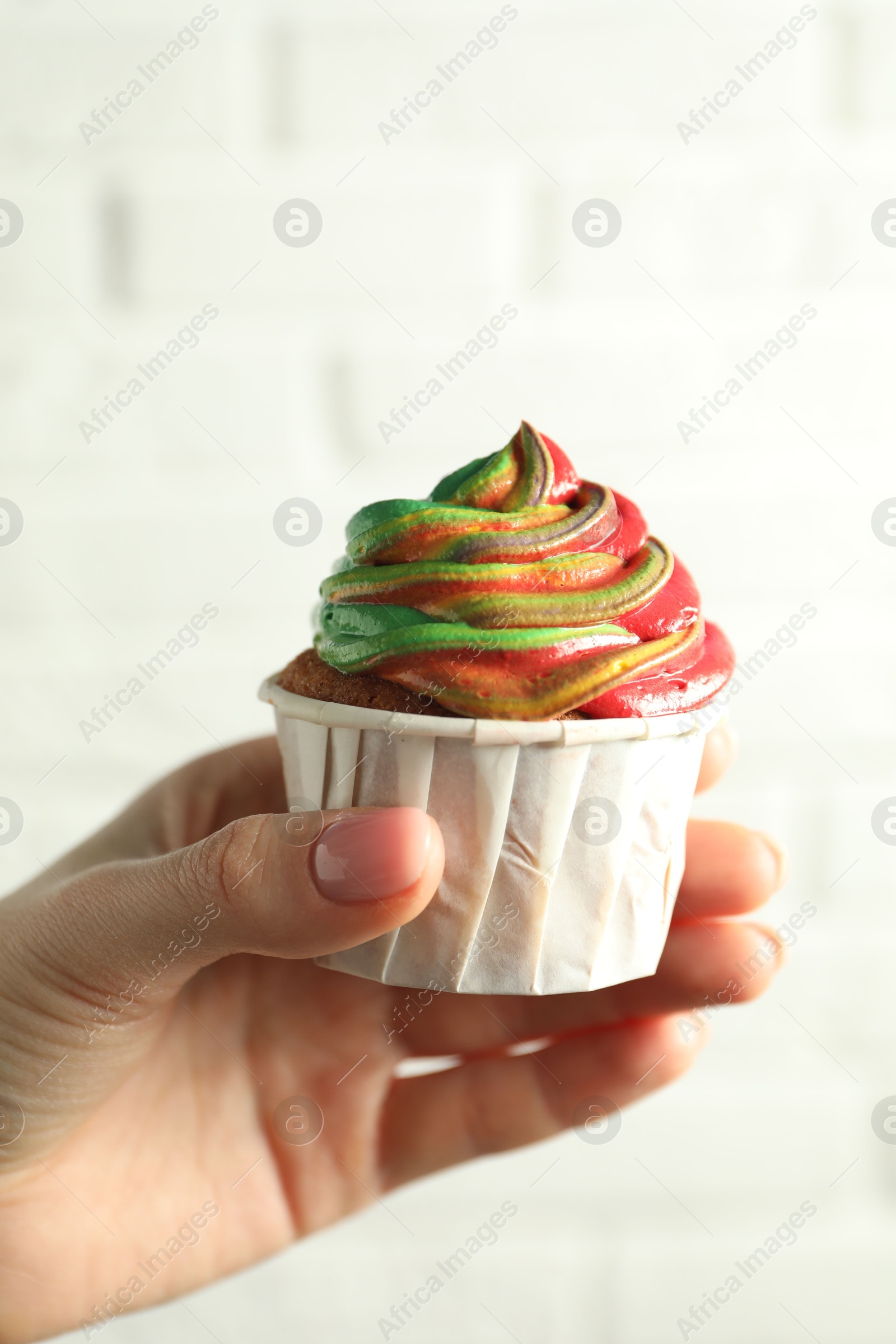 Photo of Woman holding delicious cupcake with colorful cream against white brick wall, closeup