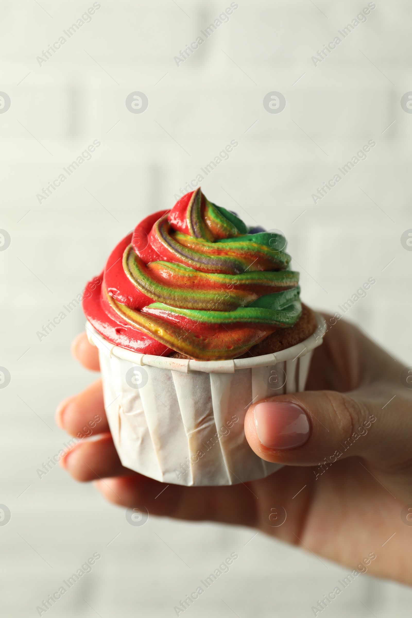 Photo of Woman holding delicious cupcake with colorful cream against white brick wall, closeup