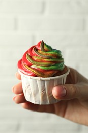 Photo of Woman holding delicious cupcake with colorful cream against white brick wall, closeup