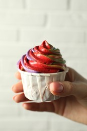 Photo of Woman holding delicious cupcake with colorful cream against white brick wall, closeup