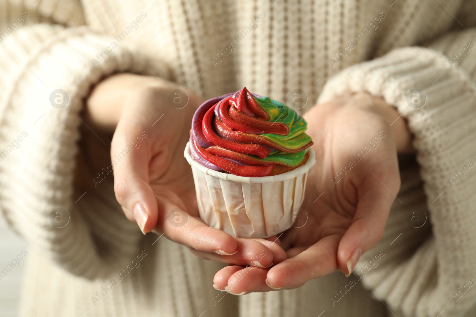 Photo of Woman holding delicious cupcake with colorful cream, closeup