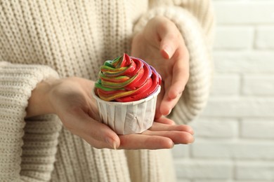 Photo of Woman holding delicious cupcake with colorful cream against white brick wall, closeup