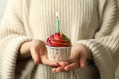 Photo of Woman holding delicious cupcake with colorful cream and burning candle, closeup